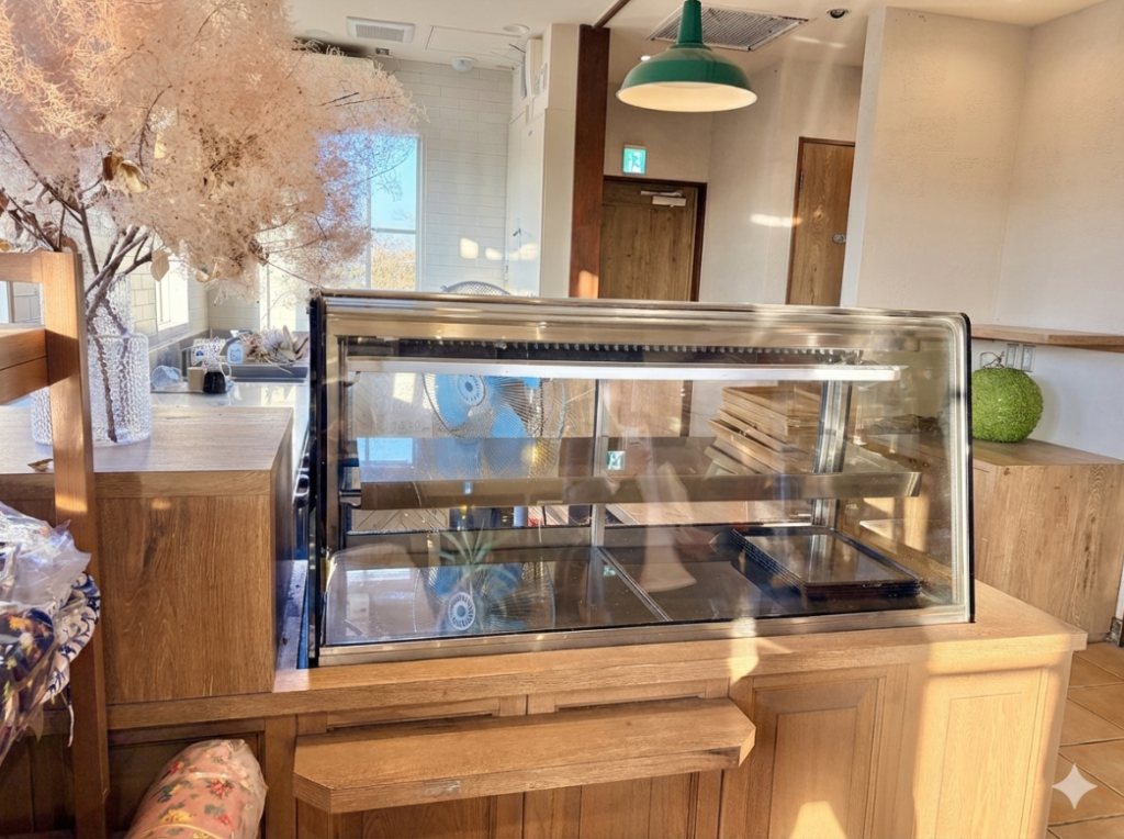 温かみのある木製カウンターに設置された、飲食店用のガラスショーケース。グリーンのペンダントライトがアクセントになった、ベーカリーやカフェの居抜き物件に適した清潔感のある内装。