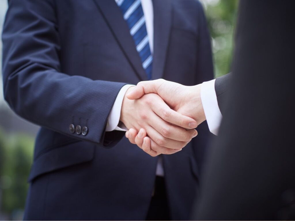 紺のスーツを着たビジネスパーソン同士が屋外で握手を交わすクローズアップ写真。ビジネスの提携や信頼関係を表現。