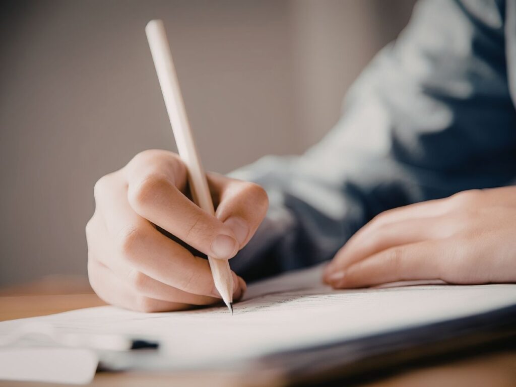 バインダーに挟まれた書類に、鉛筆で文字やサインを記入している人の手元のクローズアップ。