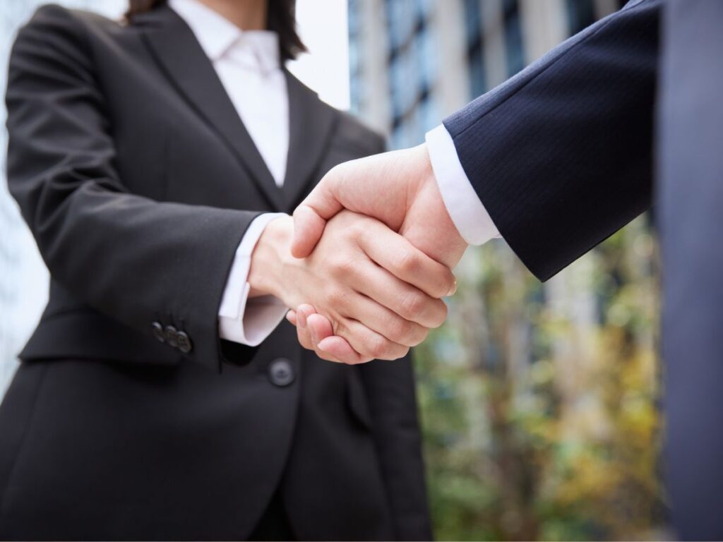企業の戦略的パートナーシップやM&Aの成立を象徴する、スーツを着た2人のビジネスパーソンの握手のアップ